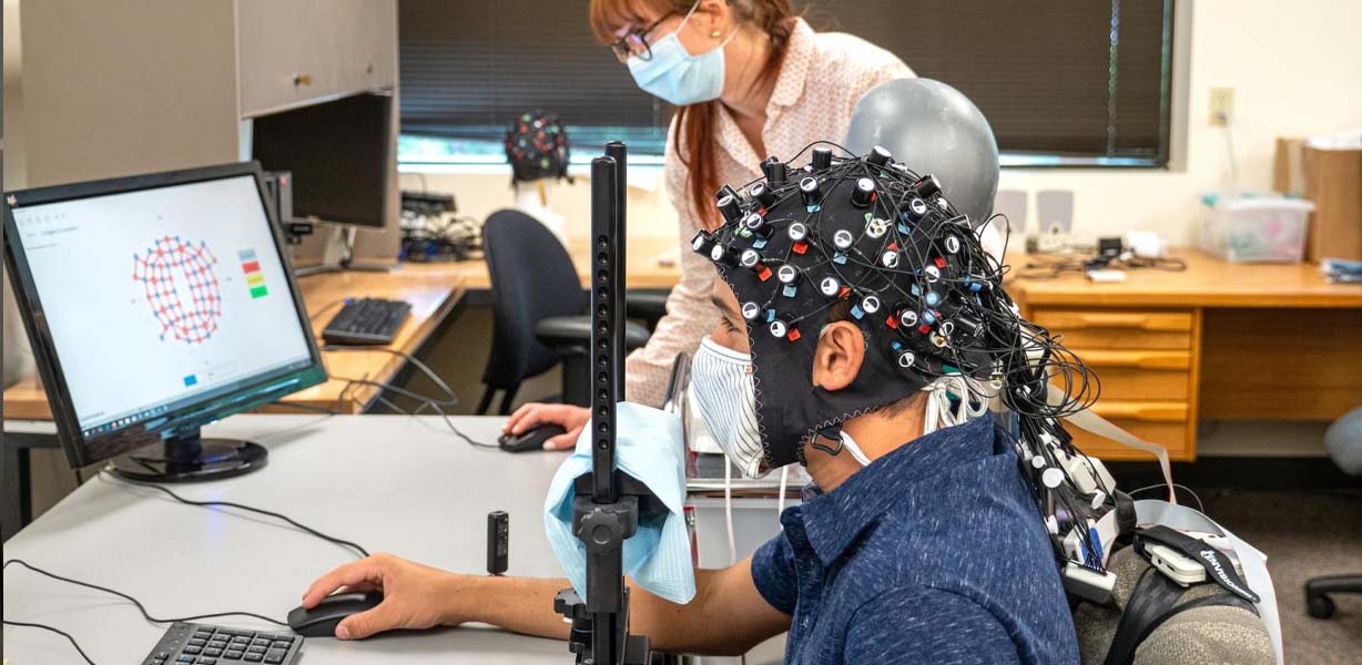 CU Boulder postdoctoral researcher Rosy Southwell and undergraduate student Cooper Steputis demonstrate a functional near-infrared spectroscopy device, which can monitor brain activity. Such lab studies will complement efforts that a university research t