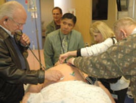 Joey Failma, simulation director for the Center for Advancing Professional Excellence at the Anschutz Medical Campus, watches as members of the South Metro Chamber of Commerce listen through stethoscopes to the internal organs of a lifelike mannequin.